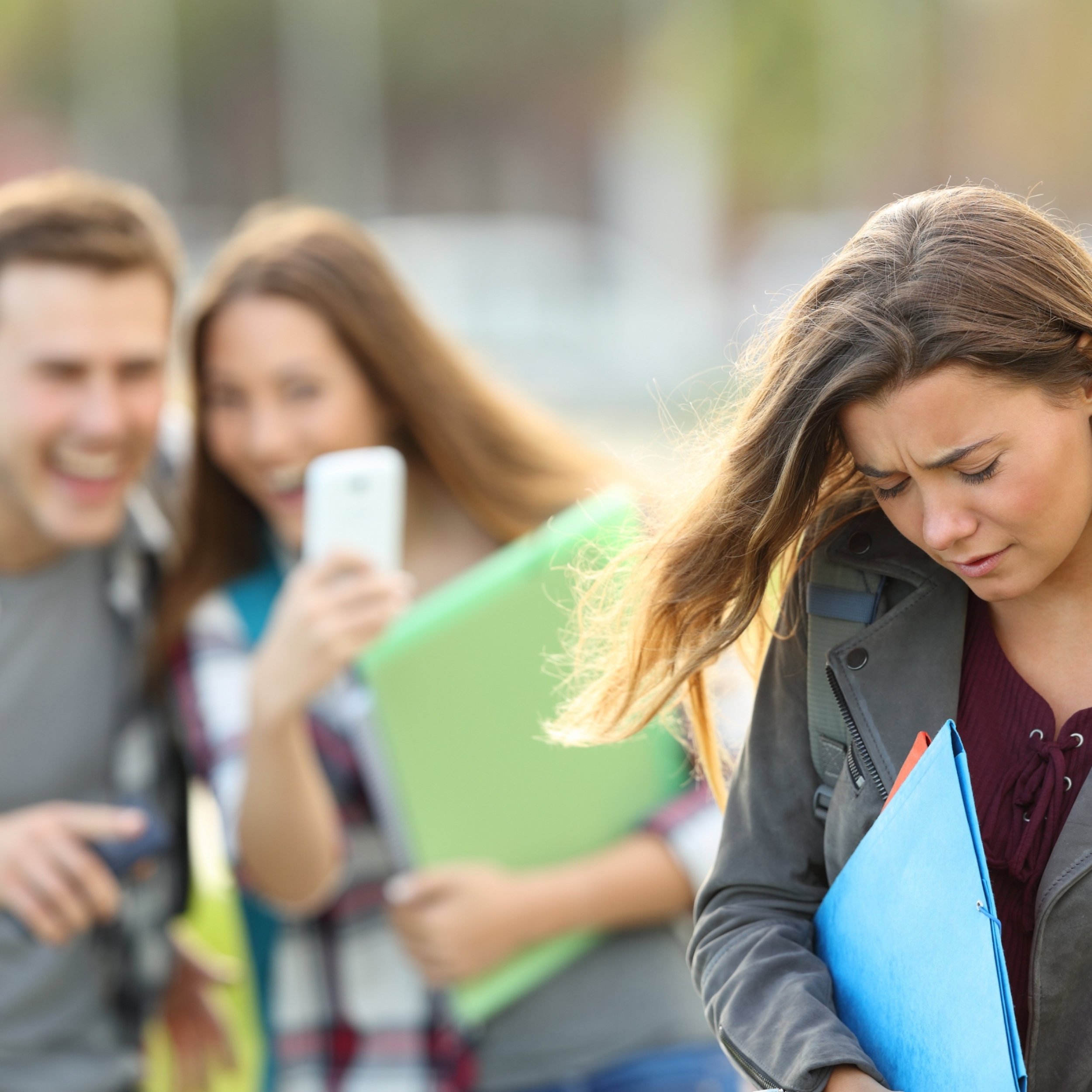 Bullying victim being video recorded on a smartphone by classmates in the street with a unfocused background